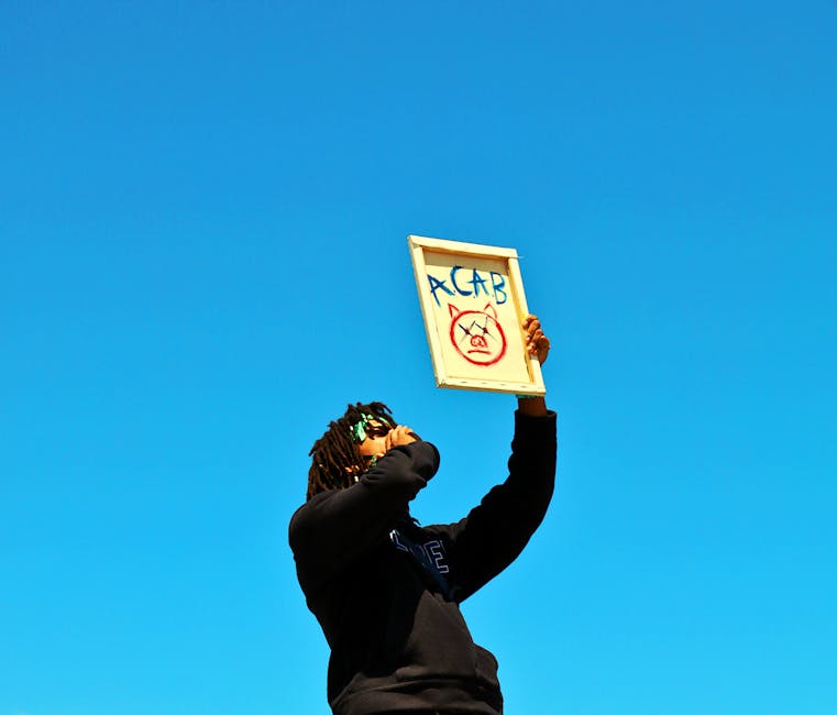 A protester raises a sign during a demonstration in Los Angeles under a clear blue sky.