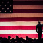 A solemn moment as a soldier salutes the American flag during a ceremony inside an auditorium.