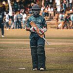 Cricketer with helmet and bat ready to play on the field during a sunny day match.