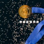 A gold medal with a blue ribbon on a black surface with glitter, symbolizing success.