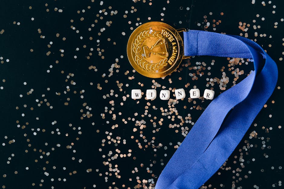 A gold medal with a blue ribbon on a black surface with glitter, symbolizing success.