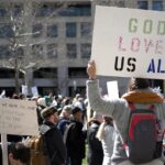 A crowd gathers for a protest in Baltimore holding signs promoting love, equality, and constitutional rights.