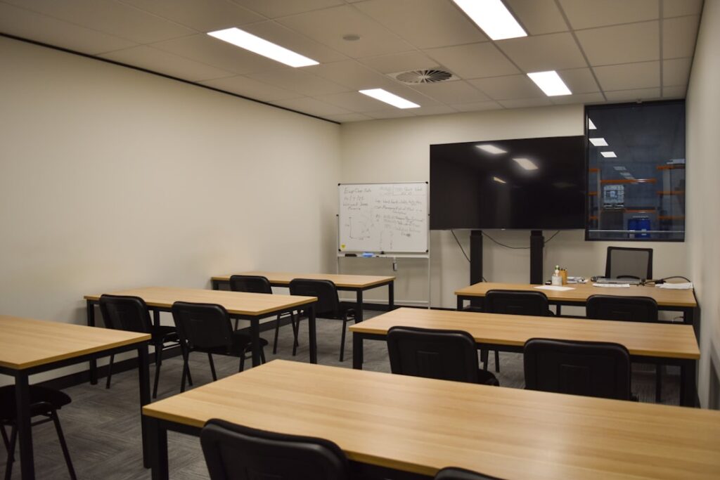A classroom with tables, chairs, and a large screen.