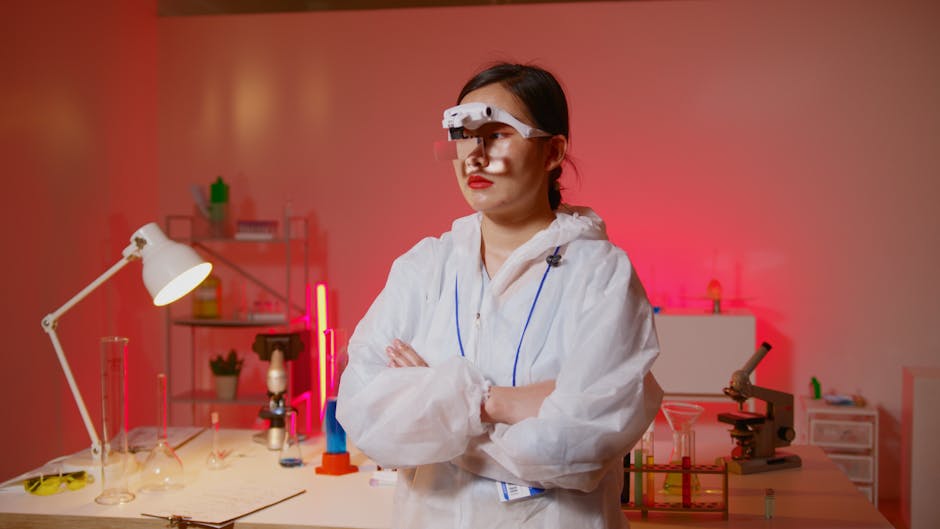 Female scientist wearing headband magnifier in lab coat, standing in modern laboratory with test tubes.