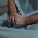 Close-up of a patient in a hospital setting, hands clasped, conveying emotion.