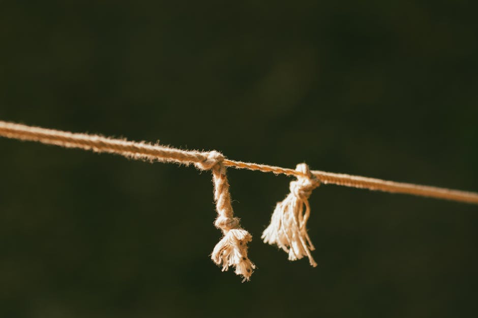 A detailed close-up of a frayed rope against a green blurred background, symbolizing tension.