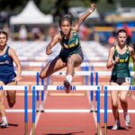 Athletes competing in a hurdle race on a track.