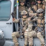 Soldiers are sitting in a helicopter doorway.