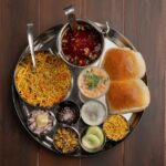 A top view of a traditional Maharashtra thali featuring spicy pav bhaji, vegetables, and condiments in Pune, India.