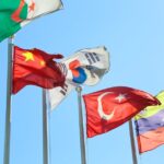 Five national flags from different countries waving on flagpoles under a clear blue sky