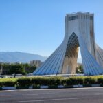 Capture of the iconic Azadi Tower in Tehran with a mountainous backdrop and clear sky.