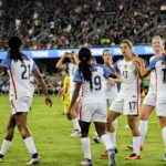 female soccer players at the field near people on bleachers