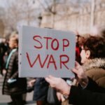 Crowd of people in a peaceful protest holding a 'Stop War' sign outdoors.
