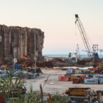 View of destruction and debris at Beirut port with cranes and sea in the background.