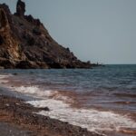 Waves crash on the rocky shore of Hormoz Island, Iran with clear blue skies.