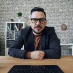 Bearded guy taking part in video conference in office talking looking at camera