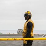 A military personnel stands on a ship's deck.