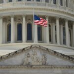 Close-up of the Capitol building in Washington DC with the US flag waving in front.