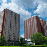 Tall brick residential buildings on a college campus under a vibrant blue sky with clouds.