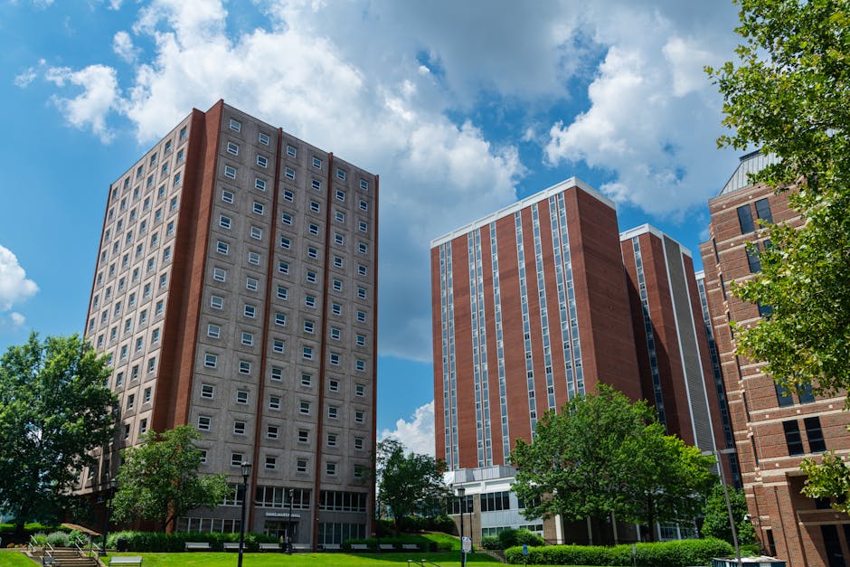 Tall brick residential buildings on a college campus under a vibrant blue sky with clouds.