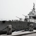 A large naval destroyer ship docked at a harbor under a gray sky.