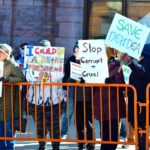 A group of people holding signs in a street protest, expressing dissent against political policies.