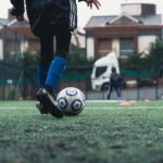 A young soccer player in blue socks practicing on an outdoor field.
