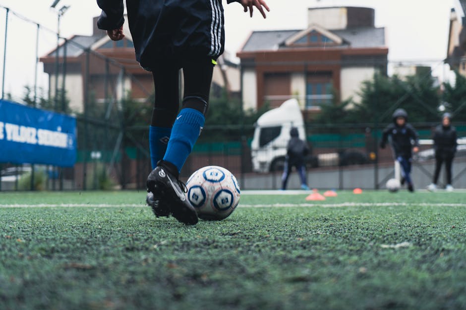 A young soccer player in blue socks practicing on an outdoor field.