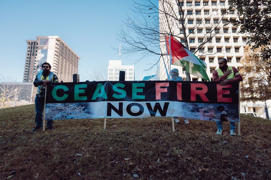 Protesters holding 'Cease Fire Now' banner in urban setting during daytime rally.