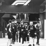 Formula 1 team members walk past the f1 logo.