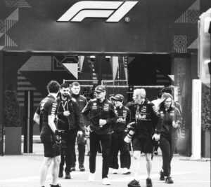 Formula 1 team members walk past the f1 logo.
