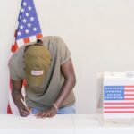 Man casting vote at polling station with American flag in background.