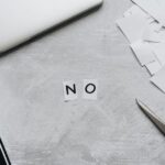 Top view of scattered paper squares, laptop, and scissors forming the word 'NO', implying rejection or denial.