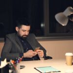 A businessman in a suit using a smartphone at his office desk at night.