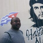 Man stands beside Che Guevara mural with Cuban flag, showcasing cultural heritage.
