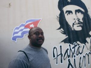 Man stands beside Che Guevara mural with Cuban flag, showcasing cultural heritage.