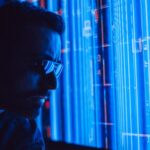 A man in sunglasses intently studies a vibrant blue holographic screen, symbolizing digital technology.