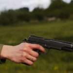 A close-up of a hand wearing a silver ring, holding a pistol outdoors.