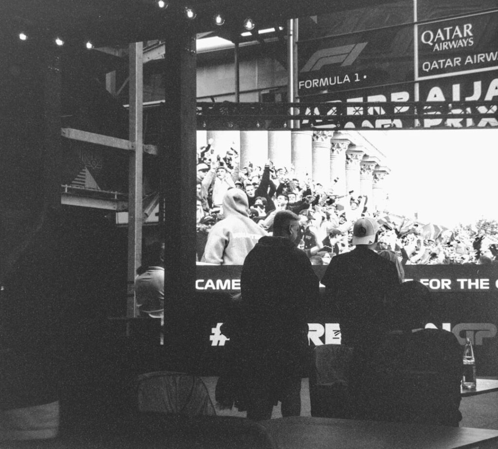 Formula 1 crowd watches screen with qatar airways advertisement.