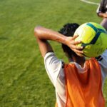 man in orange jersey shirt and white shorts holding yellow soccer ball