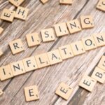 Wooden letter tiles spell 'rising inflation' symbolizing economic concerns.