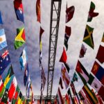 A dynamic low angle shot of various international flags hanging outdoors against a cloudy sky.