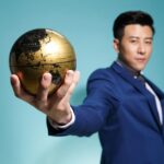 Asian businessman in blue suit confidently holding a golden globe against a blue background.