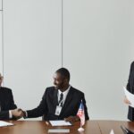 Multinational business meeting with agreement signing, featuring diverse professionals and flags.