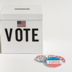 White ballot box with USA flag and 'I Voted' badges on a white background.