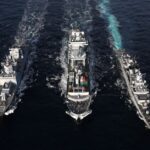 Naval ships sailing in formation on open sea, aerial view highlights naval coordination and strategy.