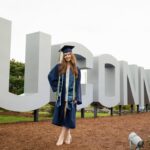 a woman in a cap and gown standing in front of a sign